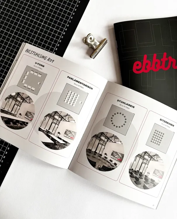 Ein aufgeschlagenes, schwarz-graues Magazin auf einem Tisch zeigt die Seite mit dem deutschen Text: "Wir sind das setzen. Wir geben deinen Ideen einen Raum."